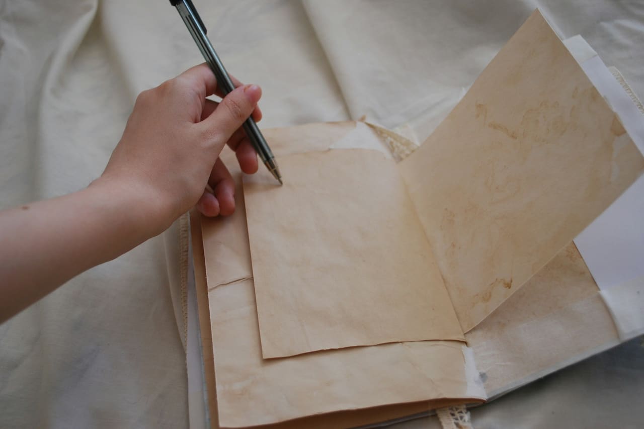 A left hand holding a pen over a sheet of aged paper